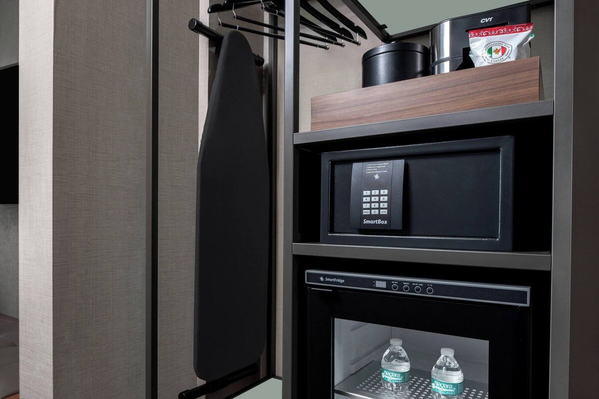 A modern hotel room with a black SmartBox, a SmartFridge, and a water dispenser.