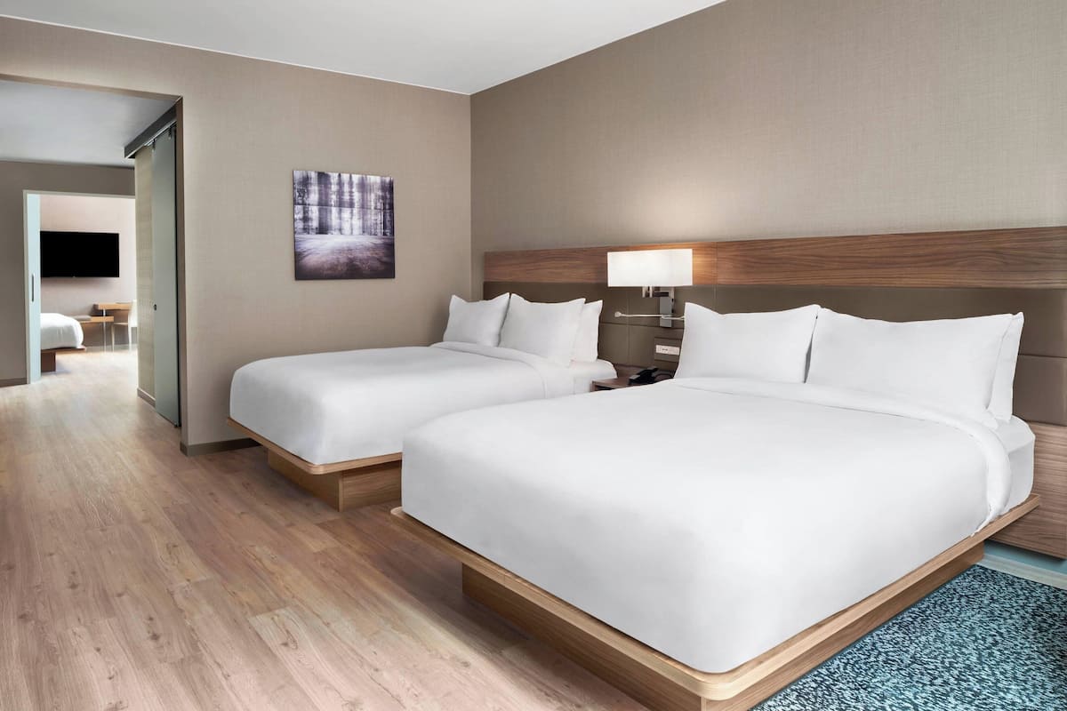A hotel room with two beds, a flat-screen TV, a painting, and a lamp.