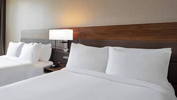 Quarto de hotel com duas camas, uma mesa de cabeceira com abajur e cabeceira de madeira.