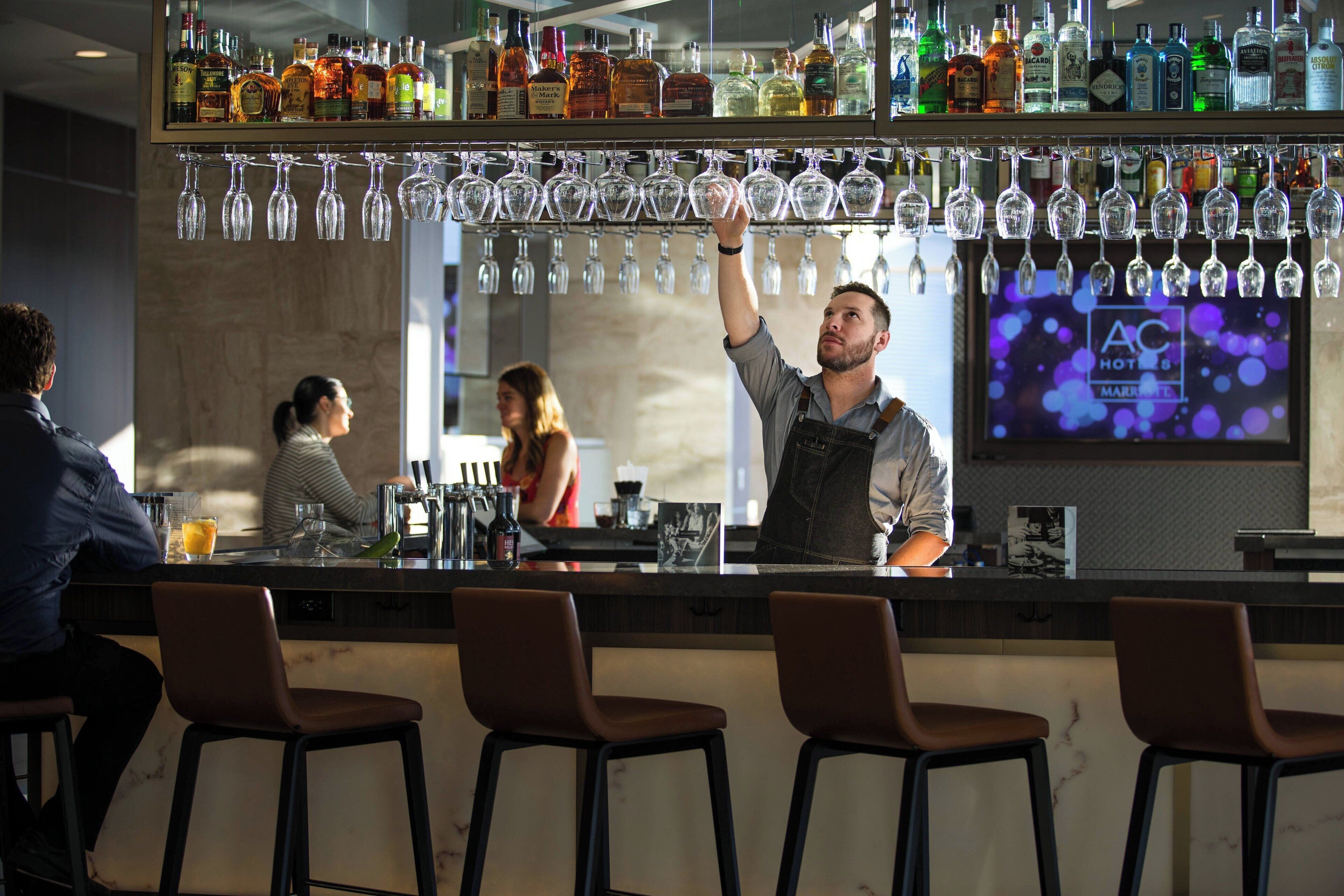 Zona de bar con varias botellas de licor, copas colgando y taburetes.