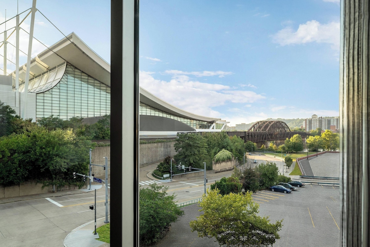 A modern building with a curved glass facade, a parking lot, and a bridge in the background.