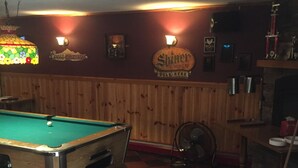 A pool table in a room with wooden paneling, a billiards cue, and a fan. - Gravity Inn Motel (Waymart)