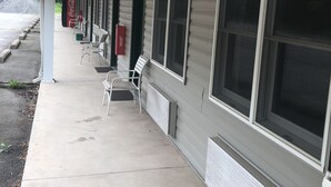 A motel with a covered walkway, rows of single-story rooms with large windows, and outdoor seating. - Gravity Inn Motel (Waymart)