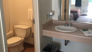 A bathroom with a toilet, sink, mirror, and a trash bin. - Gravity Inn Motel (Waymart)