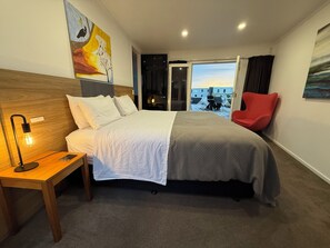 Une chambre d’hôtel avec un lit, une table de chevet avec une lampe, un fauteuil rouge et une vue sur le paysage urbain par la fenêtre.