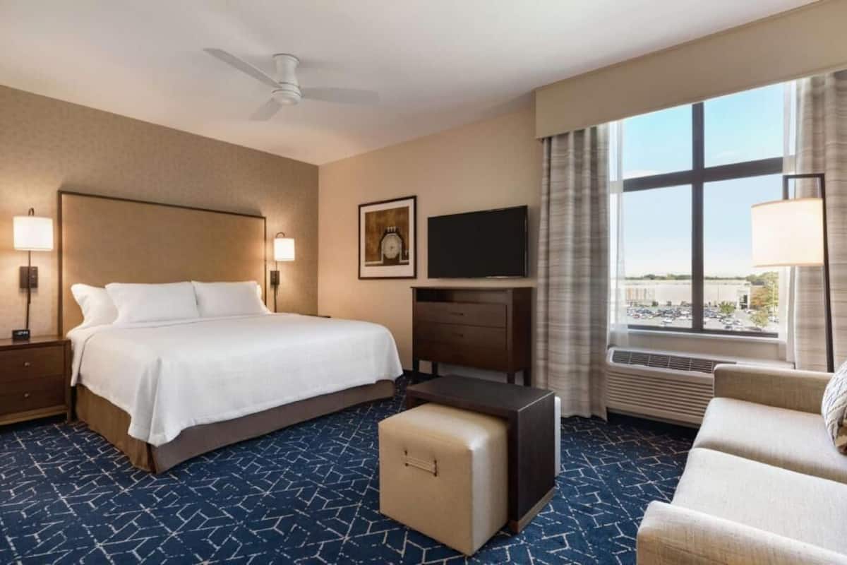 Een hotelkamer met een bed, een bureau, een televisie, een raam met uitzicht en een plafondventilator.