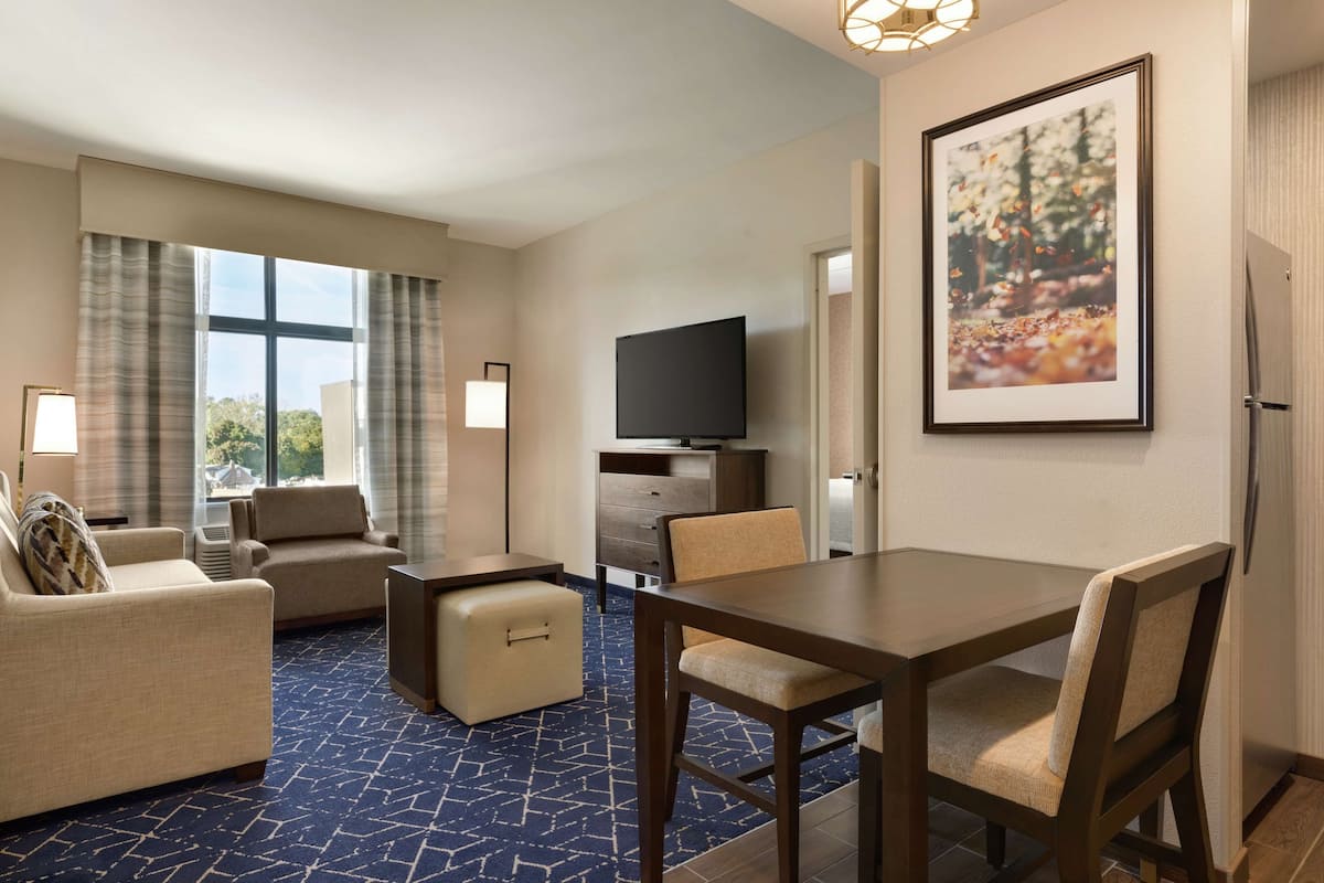 Een hotelkamer met een groot raam, een flatscreen-televisie, een eettafel met stoelen en een bank.