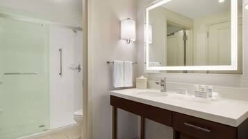 Un bagno moderno con box doccia in vetro, lavandino bianco e specchio grande, e un mobile contenitore in legno scuro.