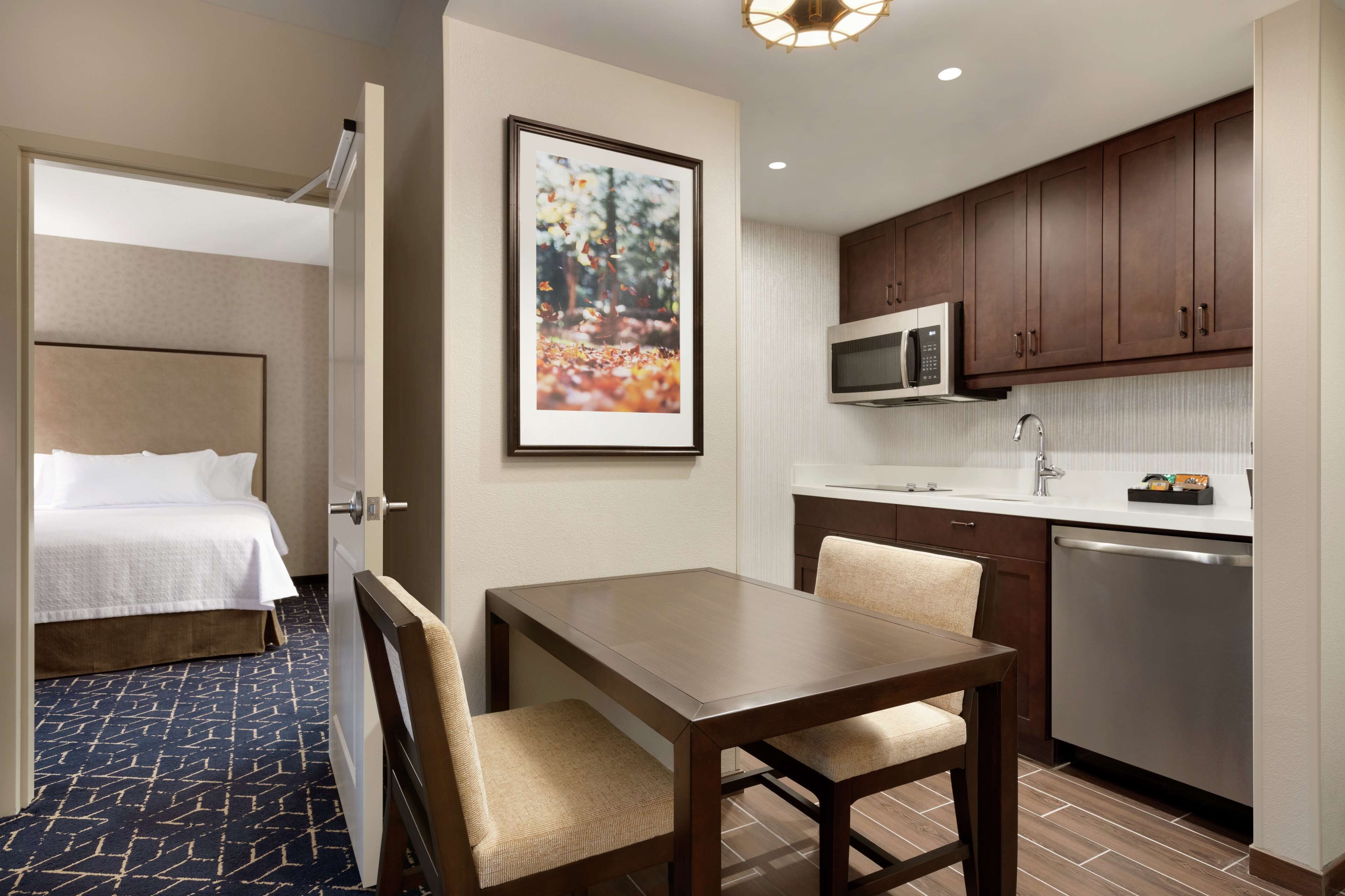 A hotel room with a bed, a dining table with chairs, a microwave, and a dishwasher.