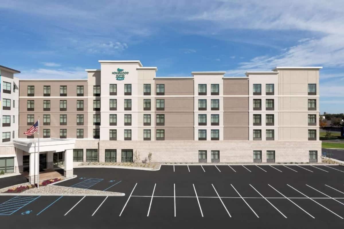 Een meerlaags hotel met een platte gevel, een parkeerplaats met aangeduide plaatsen, en een Amerikaanse vlag.