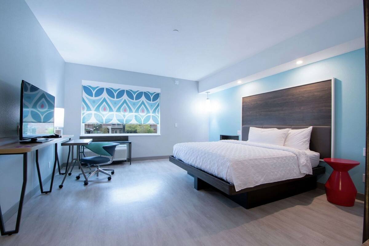 A modern bedroom with a bed, desk, chair, and a window with a view.