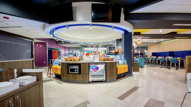 A modern restaurant with a central counter, seating area, and a projection screen on the wall.