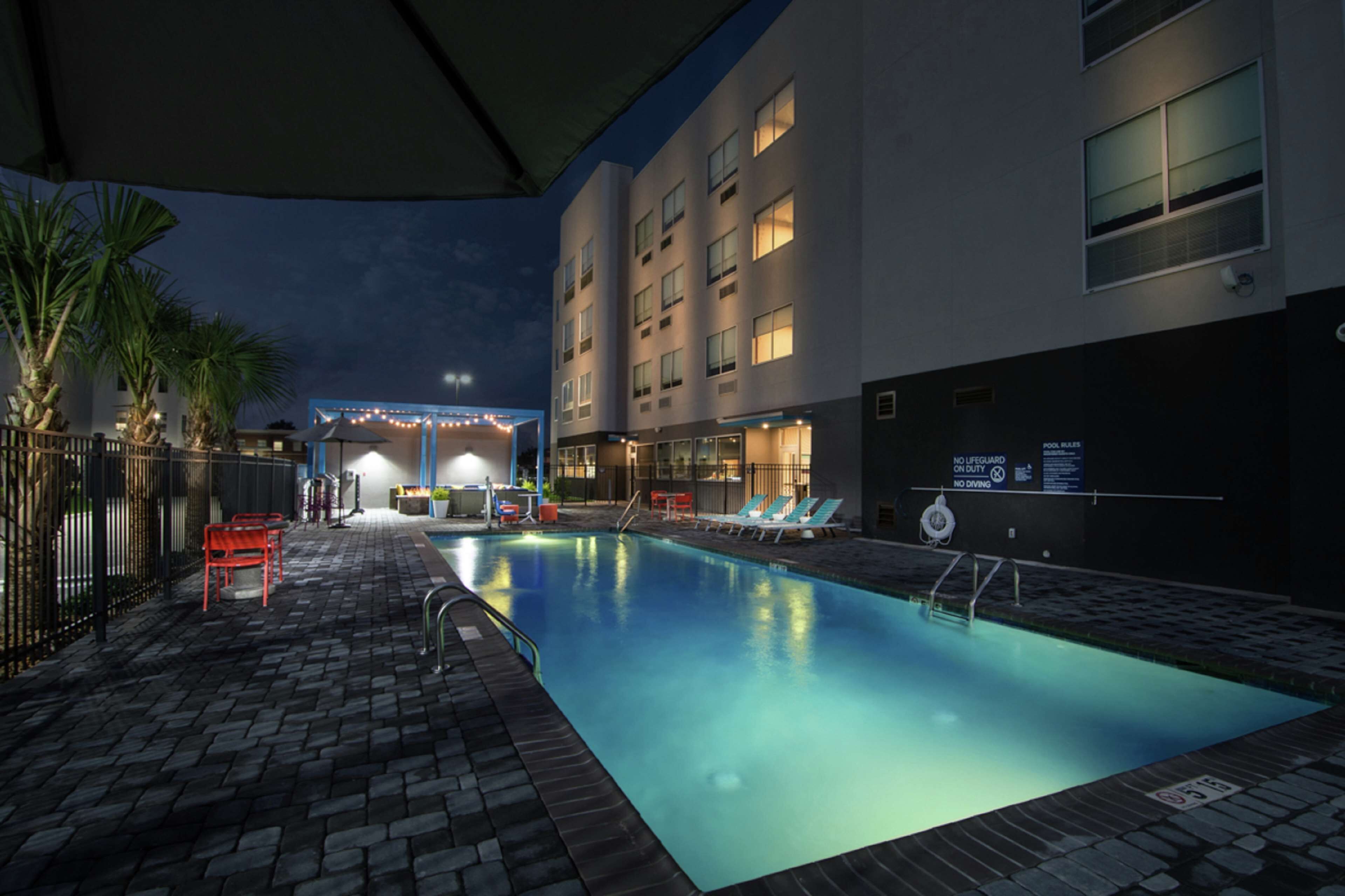 A swimming pool area with lounge chairs, a covered seating area, and a building with multiple windows.