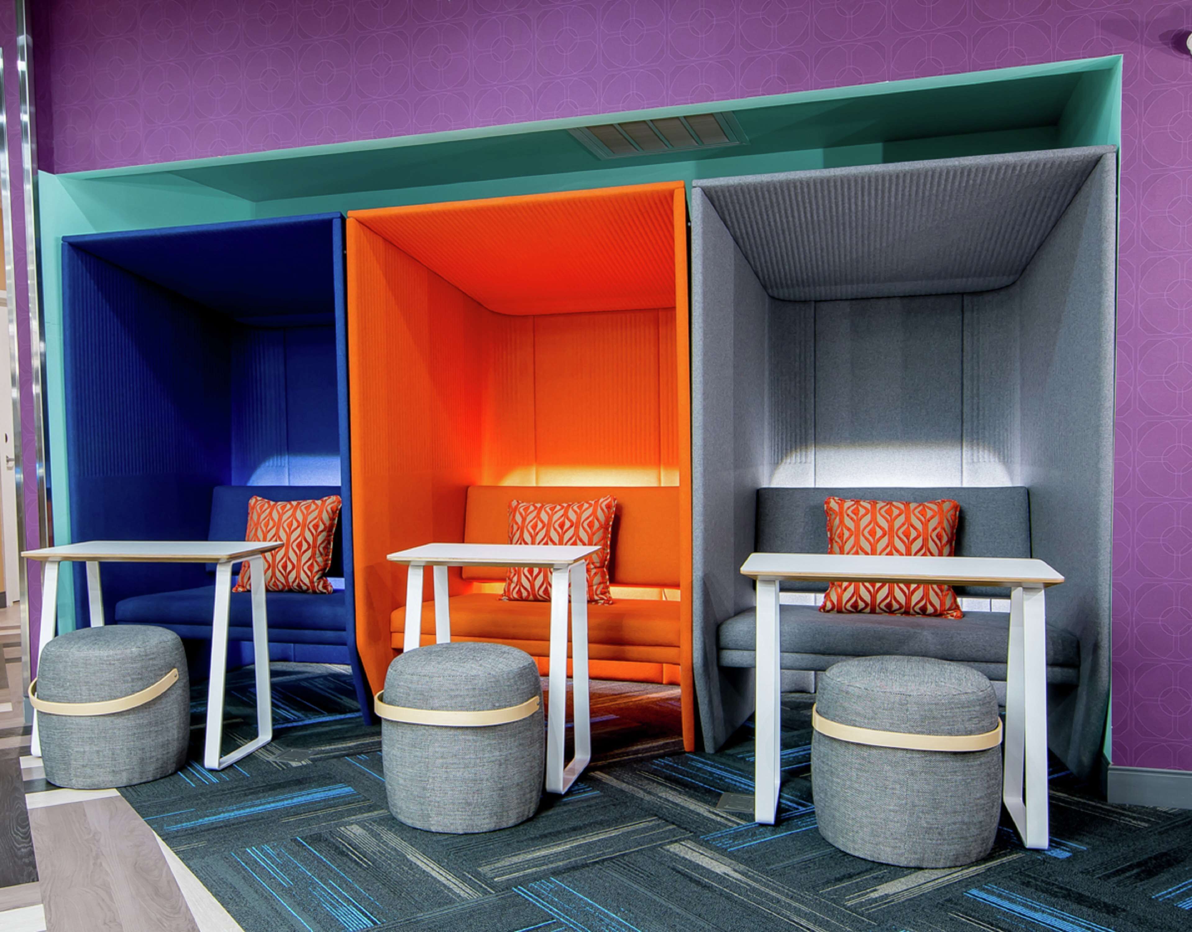 A hotel room with a vibrant color scheme, featuring orange, blue, and grey tones. It includes a sofa, two tables, and two ottomans.