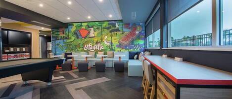 Un área lounge moderna con mesa de billar, asientos y un mural con el texto 'La Fayette'.