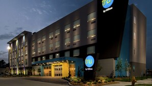 A modern hotel building with a prominent 'tru by Hilton' sign, multiple floors, and a well-lit entrance.