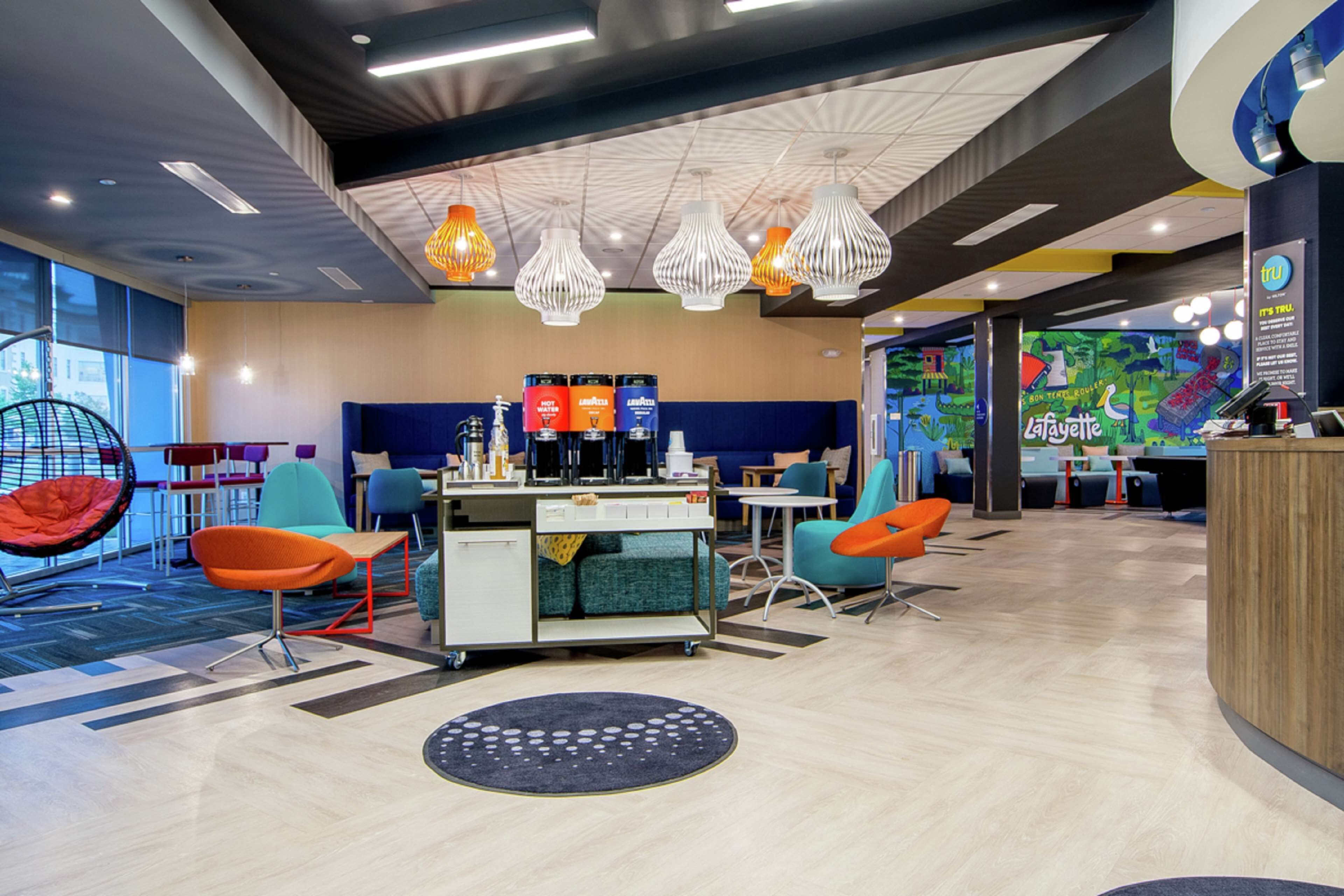 A modern lounge area with a coffee station, seating options including a hanging chair, and a mural wall.