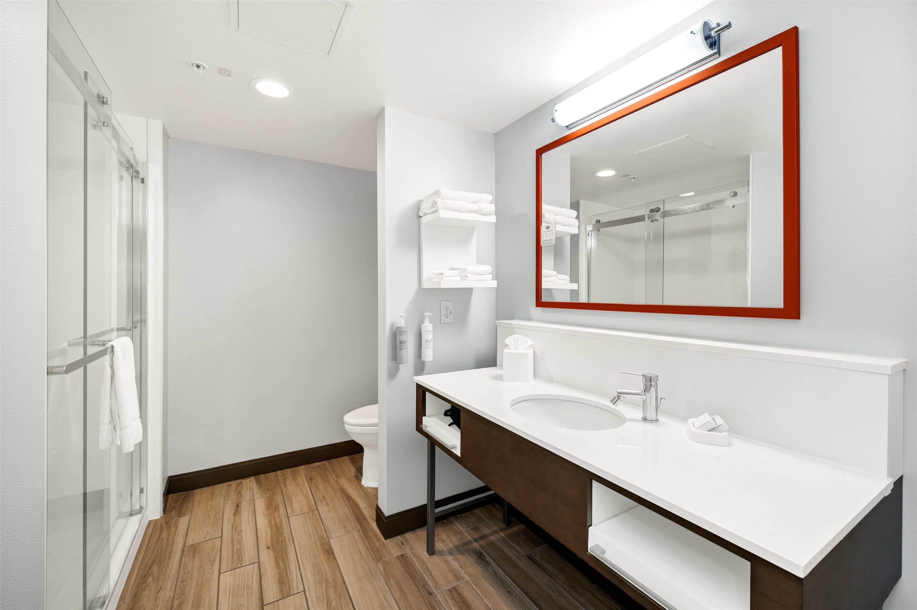 A modern bathroom with a white sink, a large mirror with a red frame, and a glass shower enclosure.