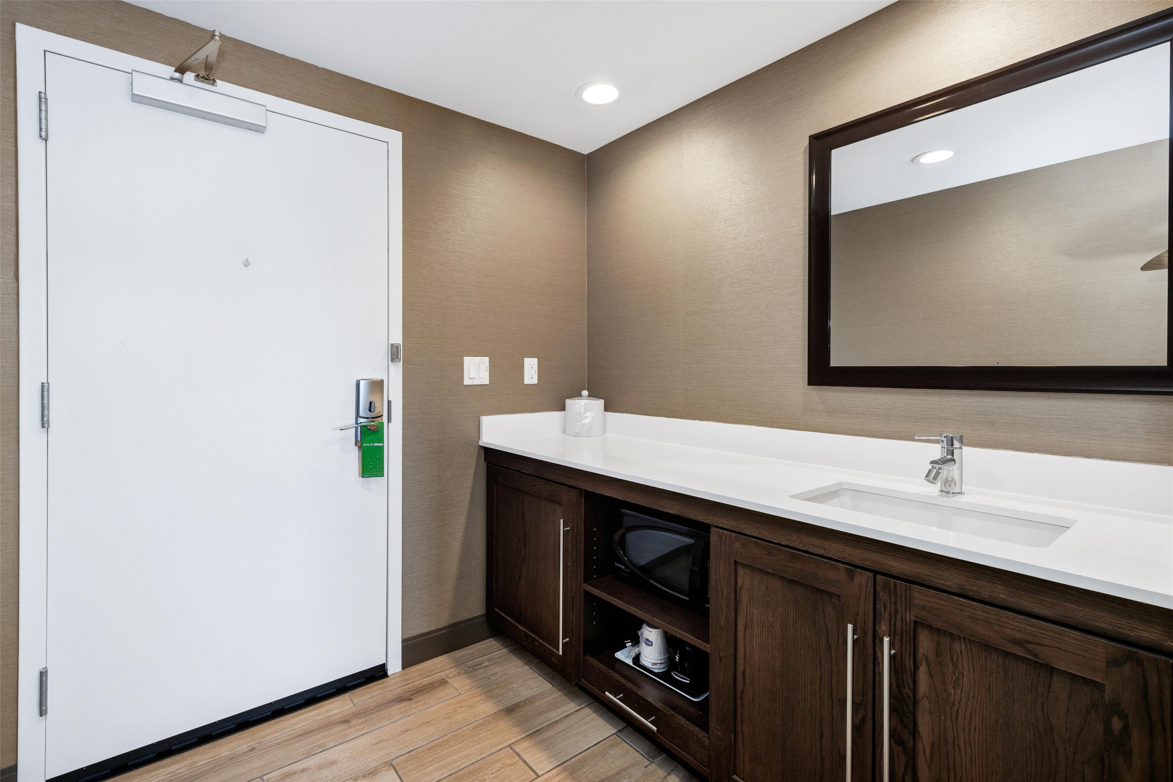 A bathroom with a white sink, dark wooden cabinets, a large mirror, and a white door.