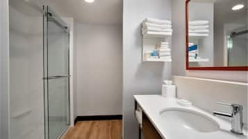 Un bany modern amb un box de dutxa de vidre, un lavabo blanc amb accessoris cromats i tovalloles ordenades sobre una estantàlia.