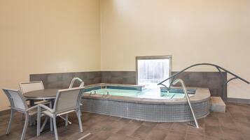 Un área de spa con un jacuzzi, una mesa con sillas y un ventanal con cortinas.