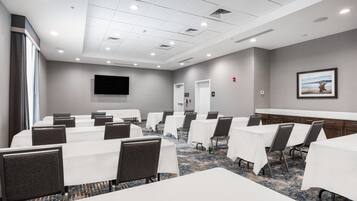 A conference room with tables and chairs, a flat-screen TV, and a carpeted floor.