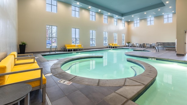 A large indoor swimming pool with yellow seating and a circular section, surrounded by large windows and a high ceiling. - Hampton Inn & Suites Logan (Logan)