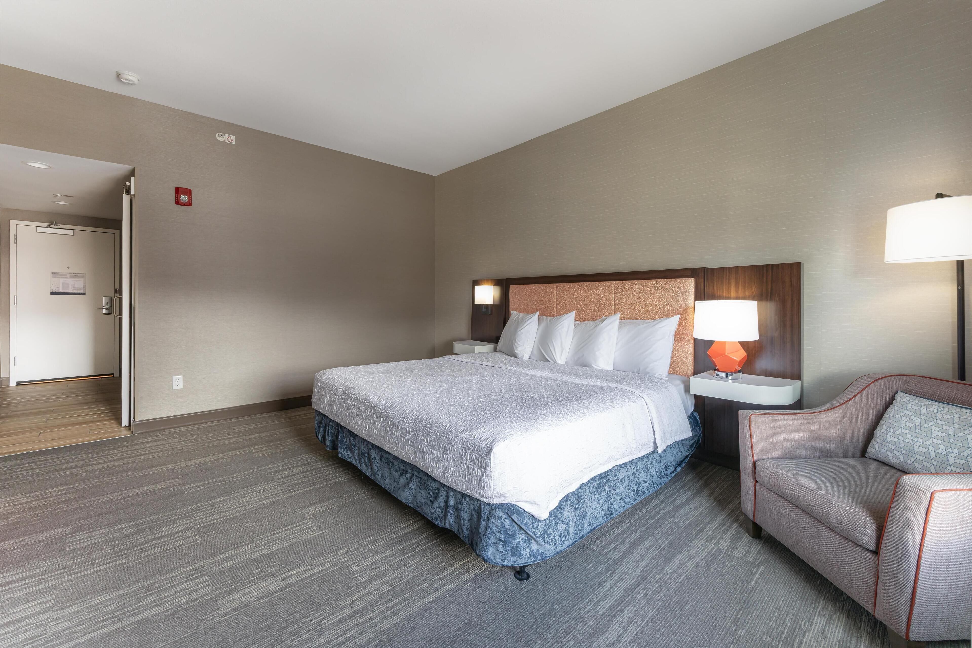 Una camera d'albergo con un letto, un comodino, una lampada e una sedia.