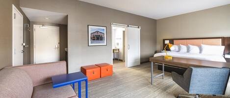 A hotel room with a bed, a desk, a chair, a sofa, and two orange storage bins.