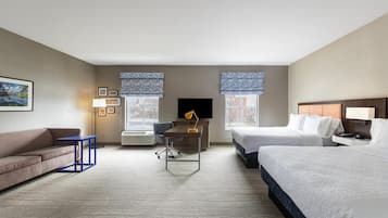 A hotel room with two beds, a desk, a chair, and a sofa.
