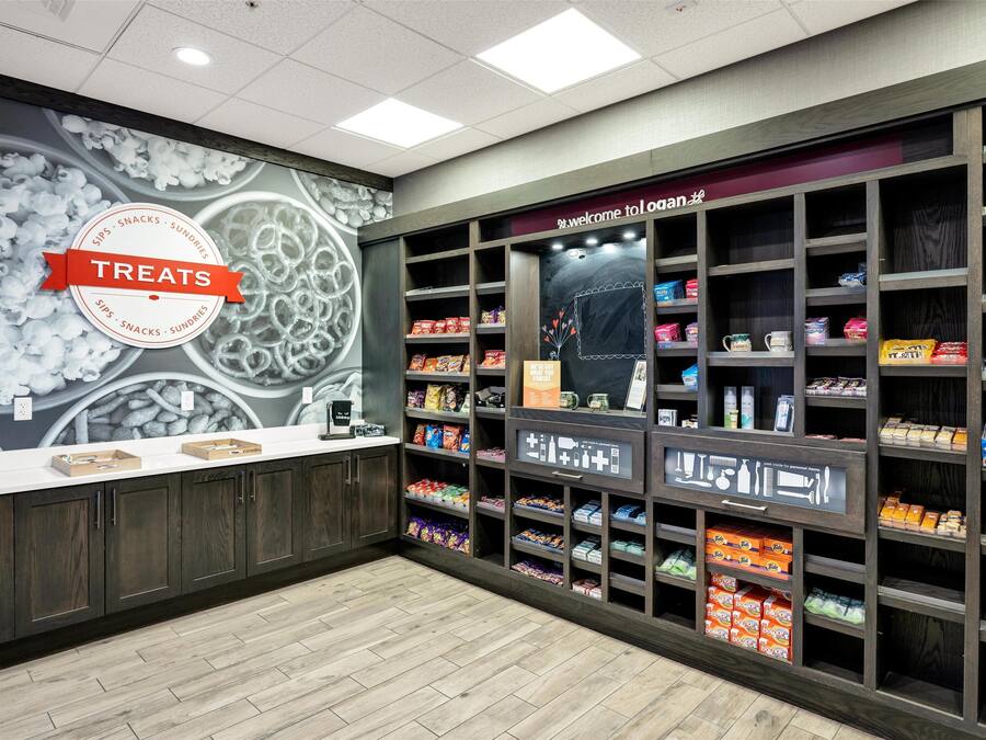 A store interior with a 'Treats' sign, shelves stocked with snacks and sundries, and a 'Welcome to Logan' sign above the entrance.
