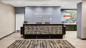 A reception area with a 'Welcome to the Bee Hive State' sign, a modern counter, and a patterned rug. - Hampton Inn & Suites Logan (Logan)