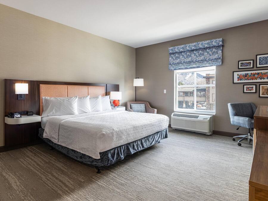 A hotel room with a large bed, bedside lamps, a desk, a chair, and a window with a view.