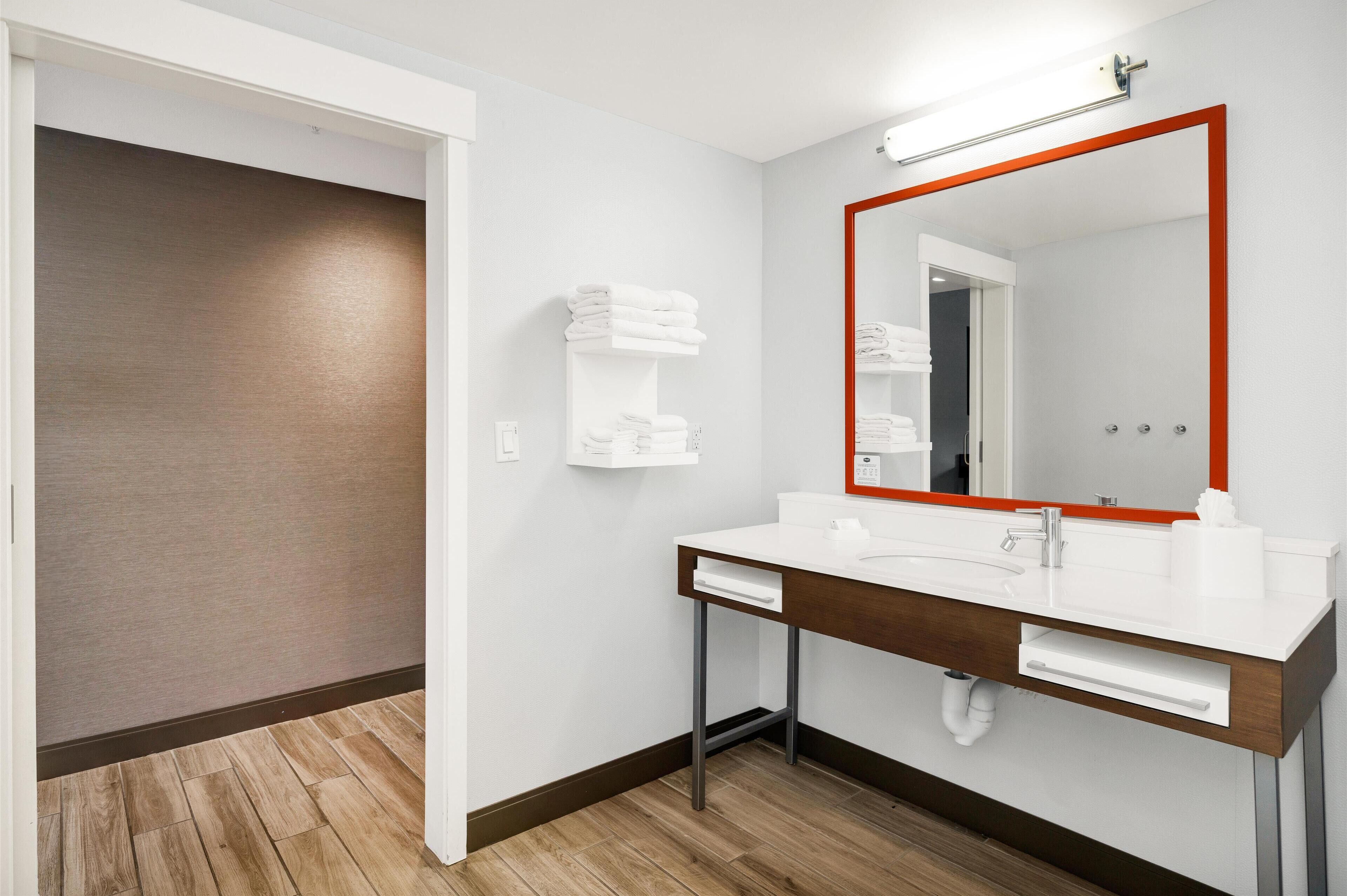 A modern bathroom with a white sink, a large mirror with a red frame, and a towel rack.