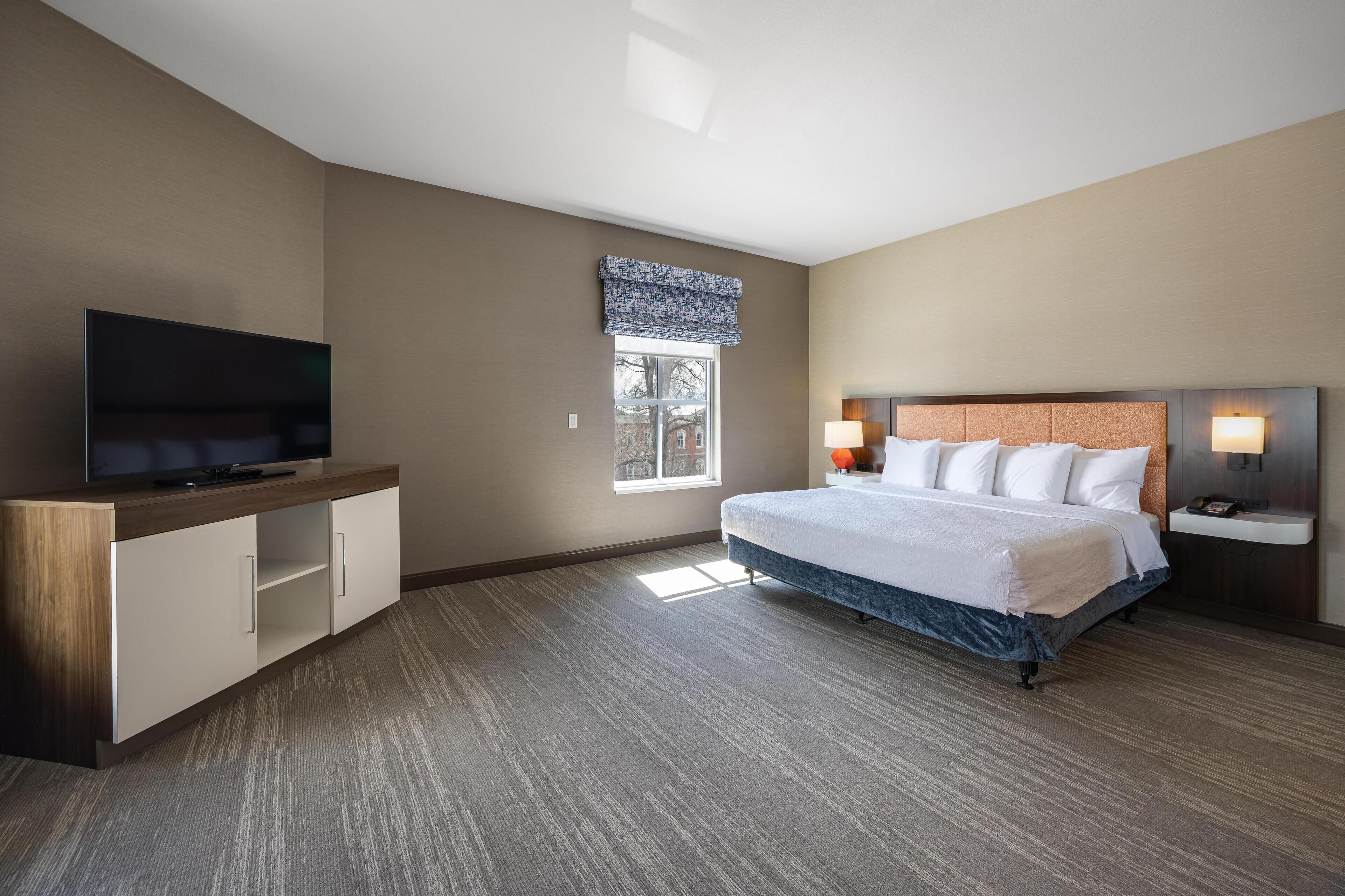 Une chambre d’hôtel avec un grand lit, un téléviseur à écran plat, une armoire en bois et une fenêtre donnant sur des immeubles.