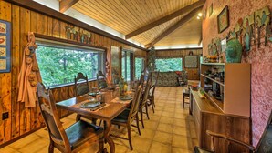 Uma sala de jantar com paredes de madeira e teto alto, com uma grande janela dando vista para árvores.