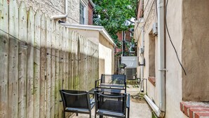 A narrow outdoor space with a wooden fence, a concrete pathway, and a table with chairs.