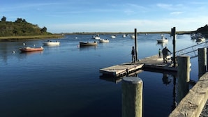 A calm harbor with several boats docked, a wooden pier, and a grassy hill in the background. - Chatham walk to Cape Cod beach  (Chatham)