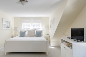 A bedroom with a white bed, two bedside tables with lamps, a television on a white dresser, and framed pictures on the walls. - Chatham walk to Cape Cod beach  (Chatham)