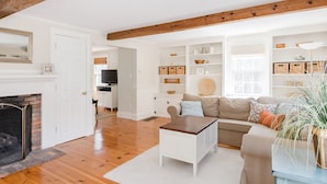 A living room with a fireplace, wooden flooring, a sofa, a coffee table, and a bookshelf. - Chatham walk to Cape Cod beach  (Chatham)