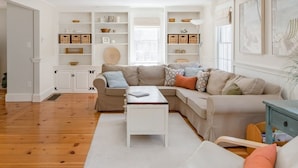 A living room with a sectional sofa, a coffee table, and built-in shelving with storage baskets. - Chatham walk to Cape Cod beach  (Chatham)
