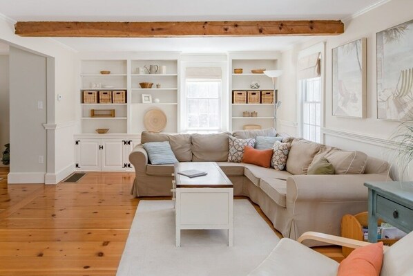 A living room with a sectional sofa, a coffee table, and built-in shelving with storage baskets. - Chatham walk to Cape Cod beach (Chatham)