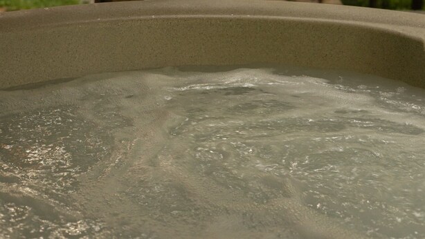 Een hottub met uitzicht op een bos en een kampvuur op de achtergrond.