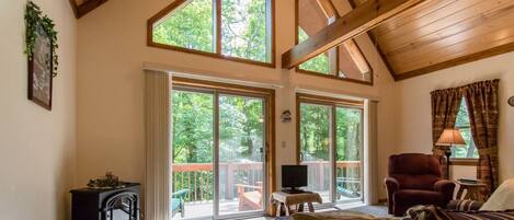 A spacious living room with a high ceiling, large sliding glass doors leading to an outdoor deck, a fireplace, and a cozy seating area.