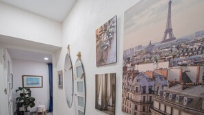 Ein Flur mit einem großen Gemälde vom Eiffelturm, einem gerahmten Stadtbild und einem Spiegel mit dekorativem Rahmen.