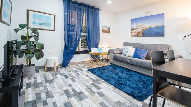 Ein modernes Wohnzimmer mit grauem Sofa, blauem Teppich und einem Essbereich mit Tisch und Stühlen.