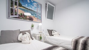 Ein Hotelzimmer mit zwei Betten, einem Strandbild, einem kleinen Tisch mit Lampe und einer Topfpflanze.