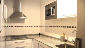 A kitchen with white cabinets, a granite countertop, a stainless steel sink, a microwave, and a range hood.