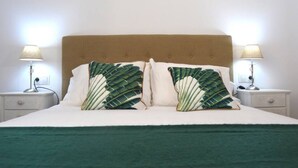 A bed with a tufted headboard, two bedside lamps, and two pillows with a tropical leaf pattern.