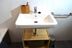 A bathroom with a white sink, wooden cabinet, and a grab bar. - Apartamento la Casa del Reloj (Cádiz)